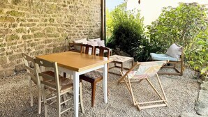 Un espacio comedor rústico al aire libre, con pared de piedra, mesa y sillas de madera, y una lámpara colgante.