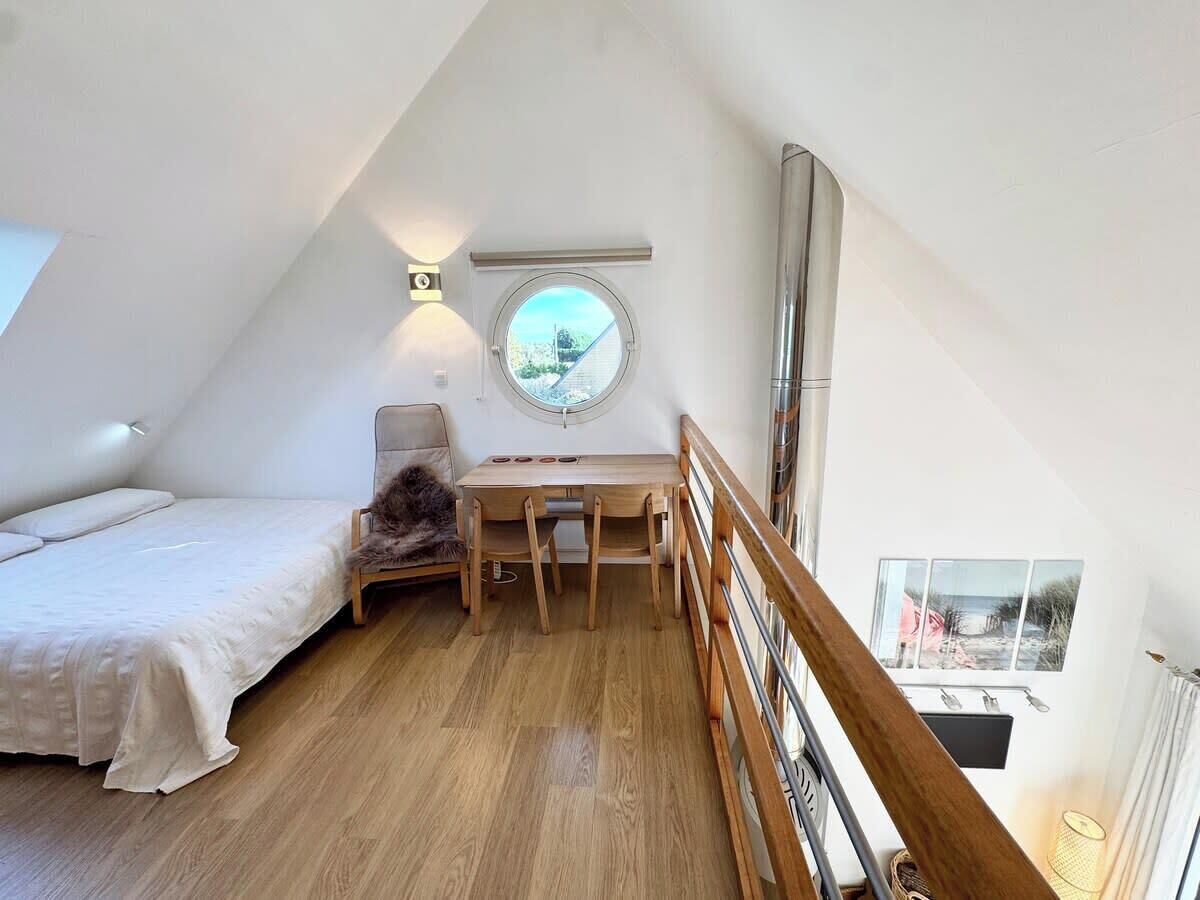 A bedroom with a bed, a desk, a chair, a round window, and a view of the outside.
