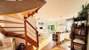 Amplia sala de estar con escalera de madera, una mesa de comedor y zona de cocina con carrito.