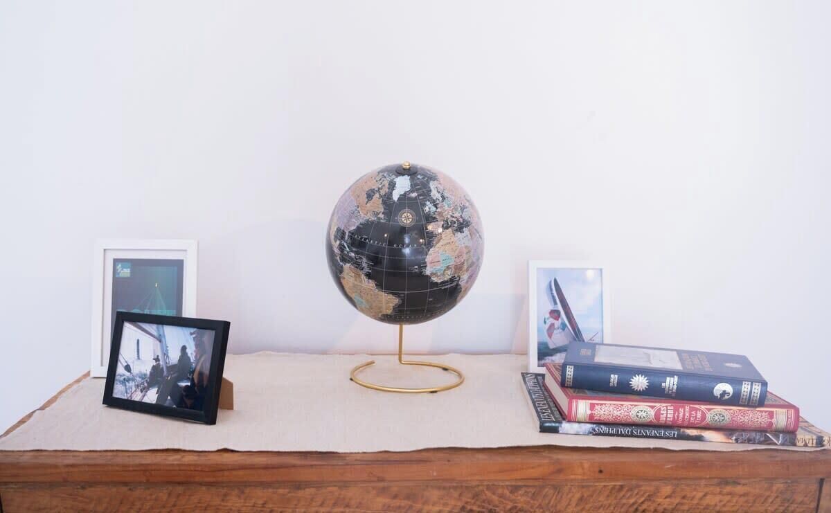 Ein Globus auf einem Ständer, umgeben von Büchern und gerahmten Fotos auf einer Holzoberfläche.