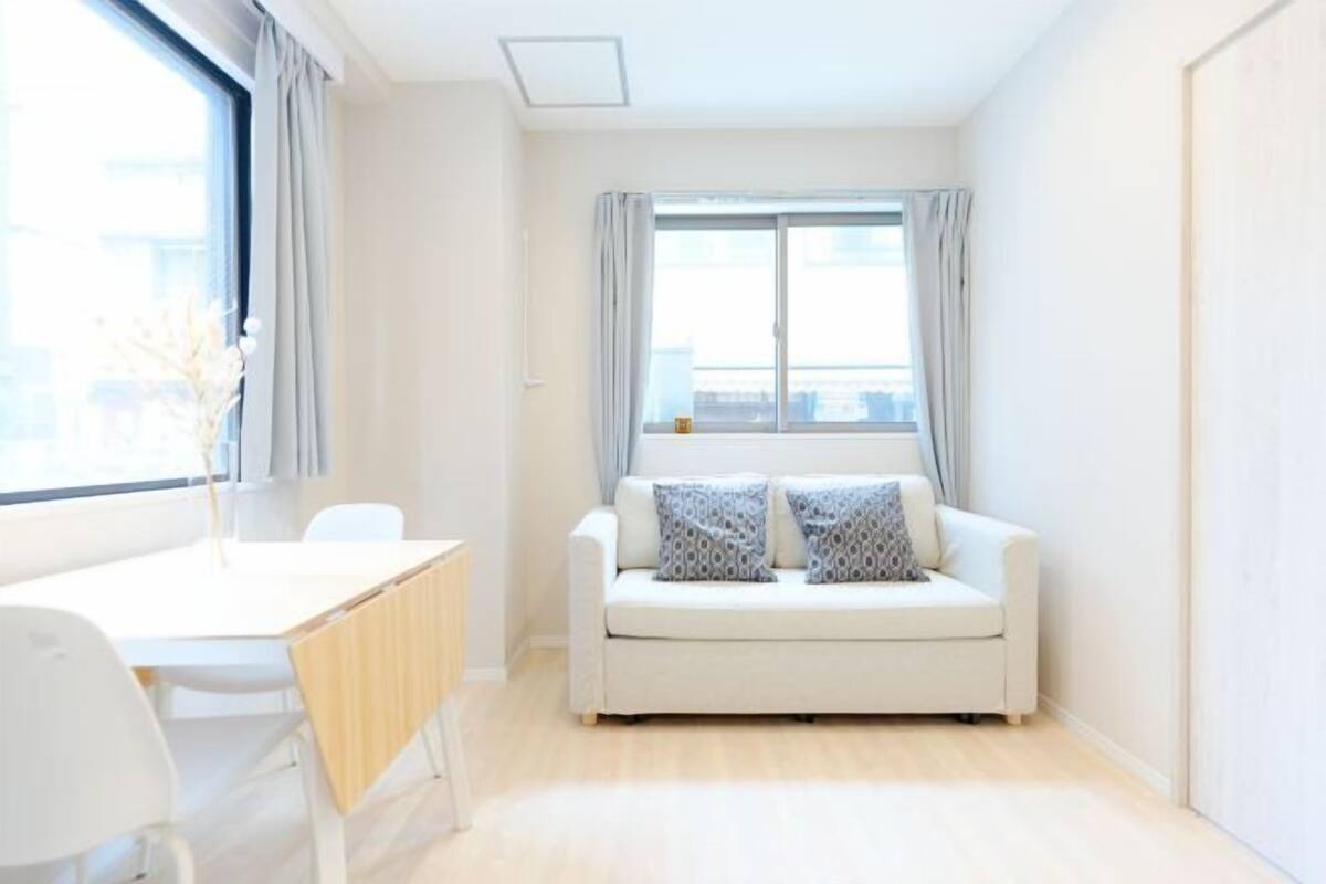 A minimalist living room with a white sofa, a small table, and a window with curtains.