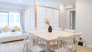 Un comedor moderno con una mesa de madera y sillas blancas, un jarrón con flores secas y un shoji corredizo al fondo.