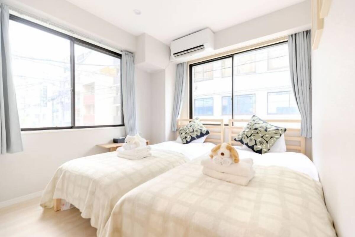 A hotel room with two beds, a window, an air conditioner, and a view of buildings outside.