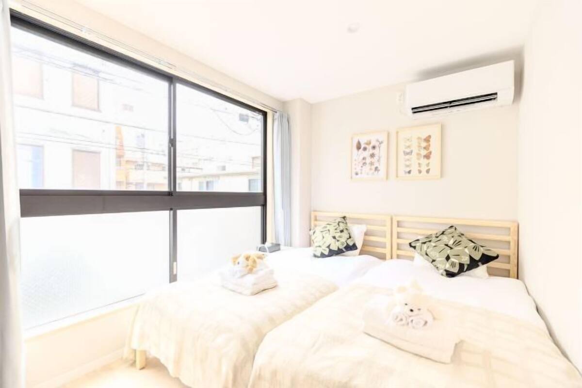 A hotel room with a large window, a bed with two pillows, and an air conditioning unit on the wall.