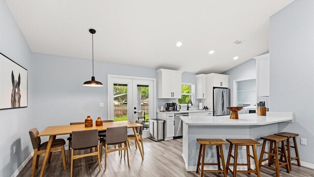 A modern kitchen with a dining area, wooden flooring, and a large island with stools.