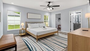A bedroom with a bed, bedside lamps, a ceiling fan, a window, and a view of the outdoors.