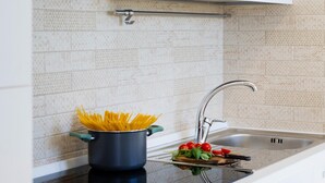 Une cuisine moderne avec des meubles blancs, un évier en acier inoxydable et une casserole de spaghettis posée sur le plan de travail.