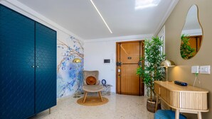 Un salon moderne avec un meuble bleu, une porte en bois, un fauteuil avec un coussin, une petite table avec une lampe et un grand miroir au mur.