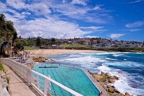A coastal swimming pool with clear blue water, surrounded by a rocky shoreline and a beach. - Comfy & Cozy Beach Studio 5min Walk to Bondi Beach (Sydney)