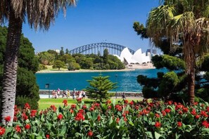 A view of the Sydney Opera House and Harbour Bridge with a park and flowers in the foreground. - Comfy & Cozy Beach Studio 5min Walk to Bondi Beach (Sydney)