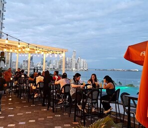 An outdoor dining area with tables and chairs, a city skyline in the background, and a view of the water. - Cozy Apartment on Avenida Balboa-panama (Panama City)