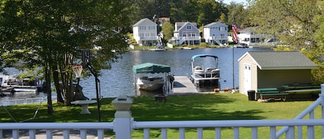 A lakeside view with a dock, boats, and houses in the background.