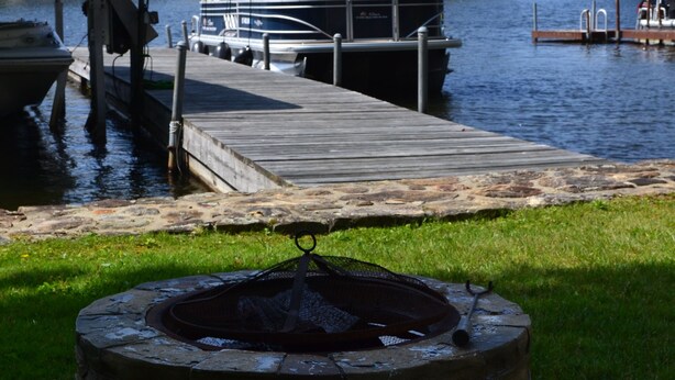 A dock with boats, a stone fire pit with American flags, and houses in the background. - Lakefront Escape on Highland (Winchester)