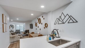 A modern kitchen with a central island, white cabinetry, and decorative wall art. - Fall Ridge Retreat | Hot Tub & Pool (Vail)