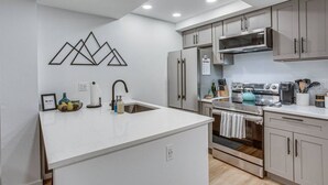 A modern kitchen with a central island, stainless steel appliances, and a geometric wall decoration. - Fall Ridge Retreat | Hot Tub & Pool (Vail)