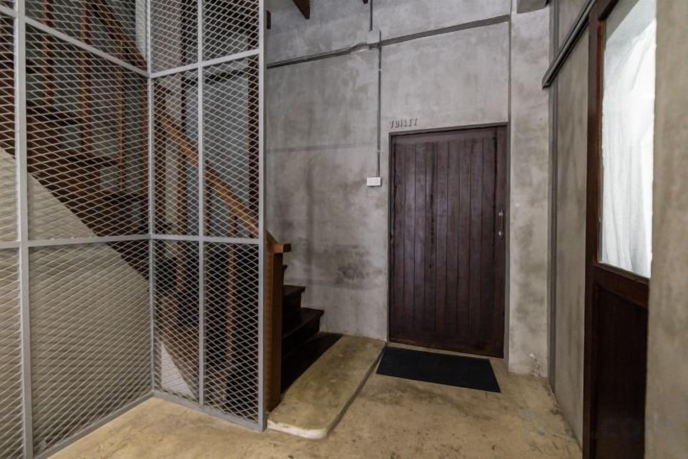 Una escalera estrecha que conduce a una puerta de madera con una barrera de malla metálica en un lado.