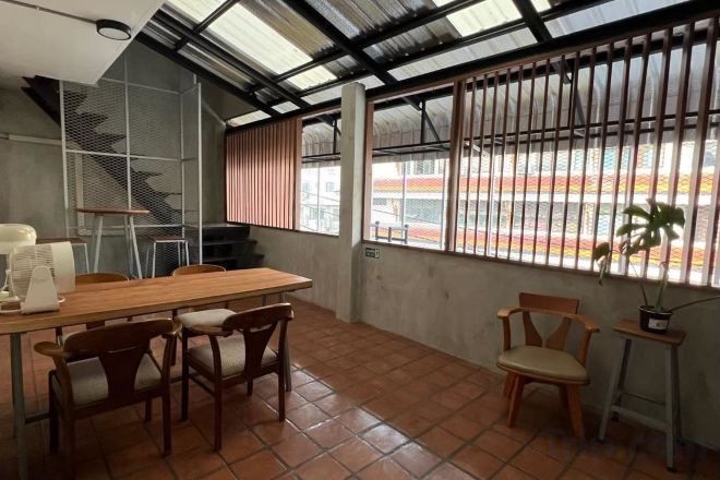 A room with a wooden table, chairs, a window with metal bars, and a view of a building outside.