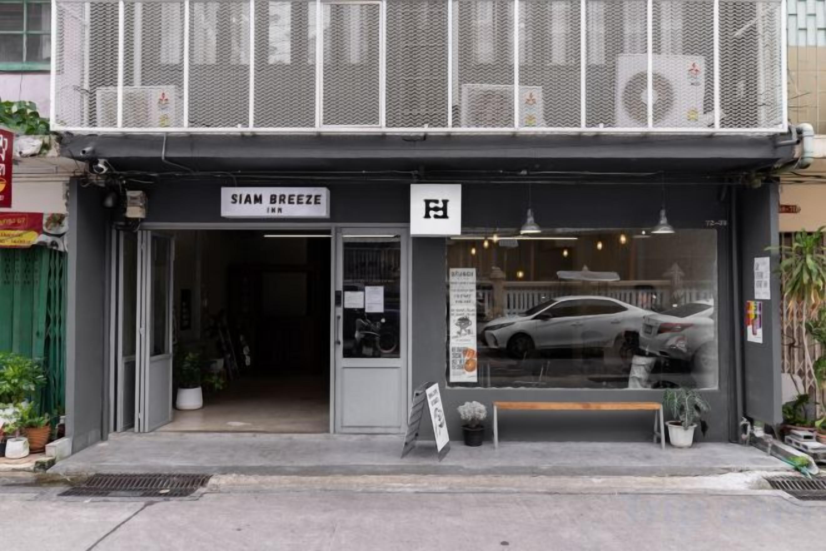 Una fachada con un letrero que dice 'SIAM BREEZE INN' y un coche estacionado frente a ella.