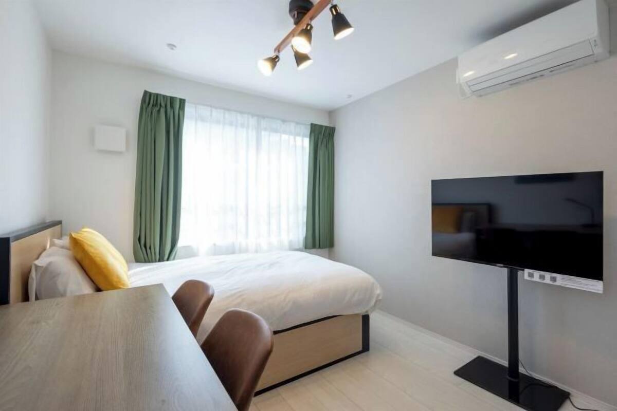 A hotel room with a bed, a TV, a desk, and a window with curtains.
