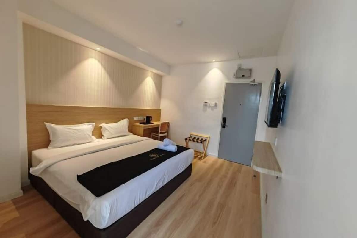 A hotel room with a large bed, a bedside table, a TV mounted on the wall, and a door leading to another room.