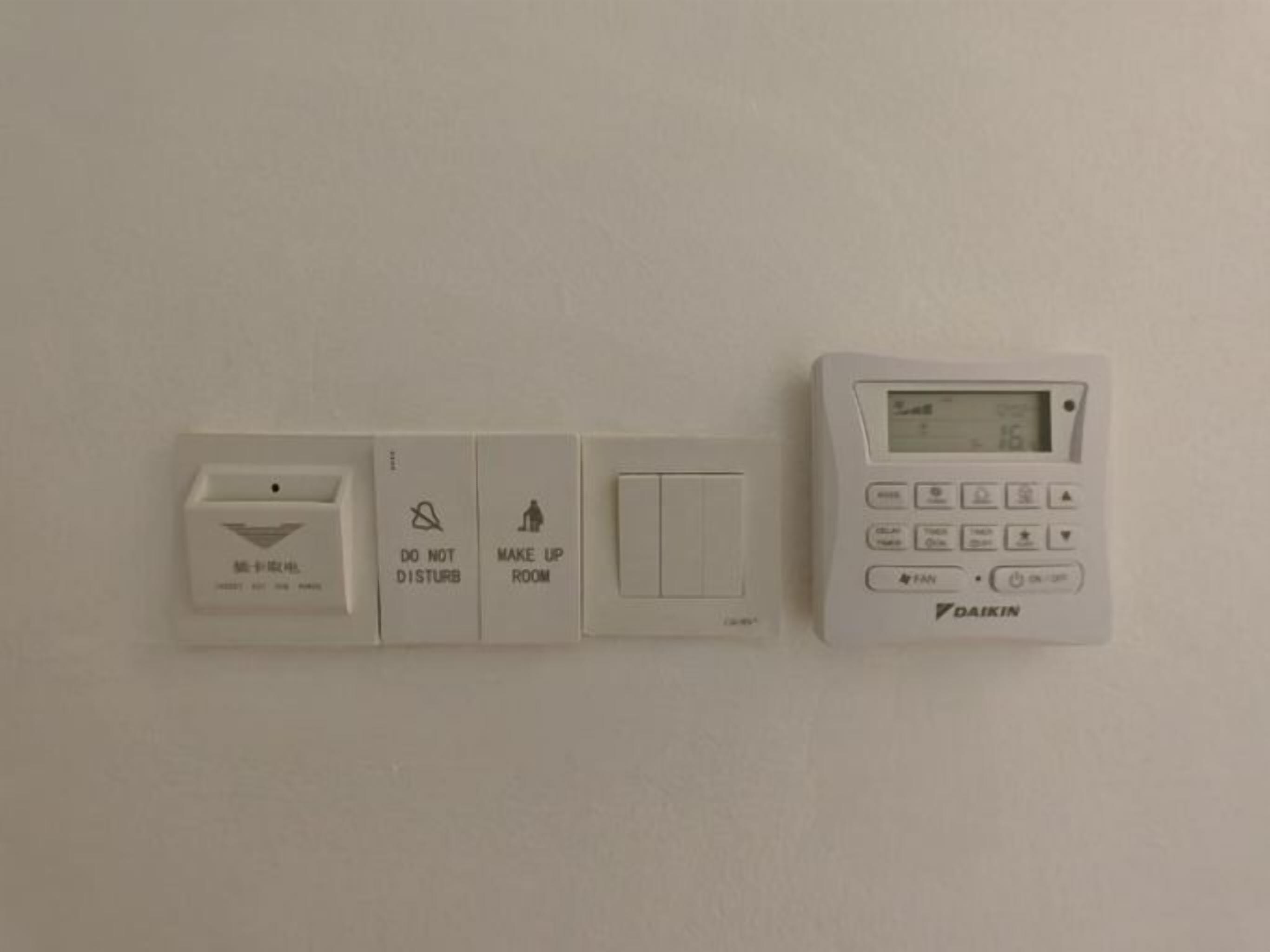 Een bedieningspaneel aan de muur met een thermostaat, een lichtschakelaar en een 'S.V.P. Niet Storen' bordje.