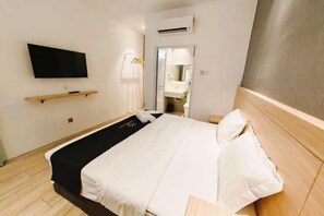 A hotel room with a bed, a TV mounted on the wall, a mirror, and a wooden headboard.