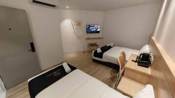 Quarto de hotel com duas camas, uma televisão e uma pequena mesa com cafeteira.