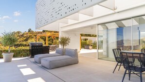 Eine moderne Außenpatio mit einer grauen Couch, einem Grill und einem überdachten Essbereich.