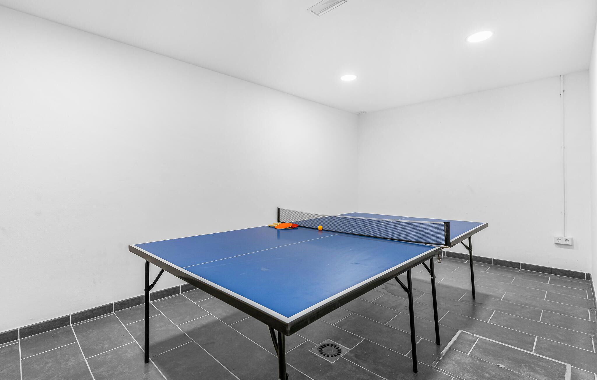 Una mesa de ping pong en una habitación con paredes blancas y suelo de baldosas grises.