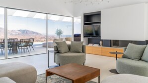 Ein modernes Wohnzimmer mit großer Glaswand, einem Flachbildfernseher und einem Essbereich mit Stühlen und Tisch.