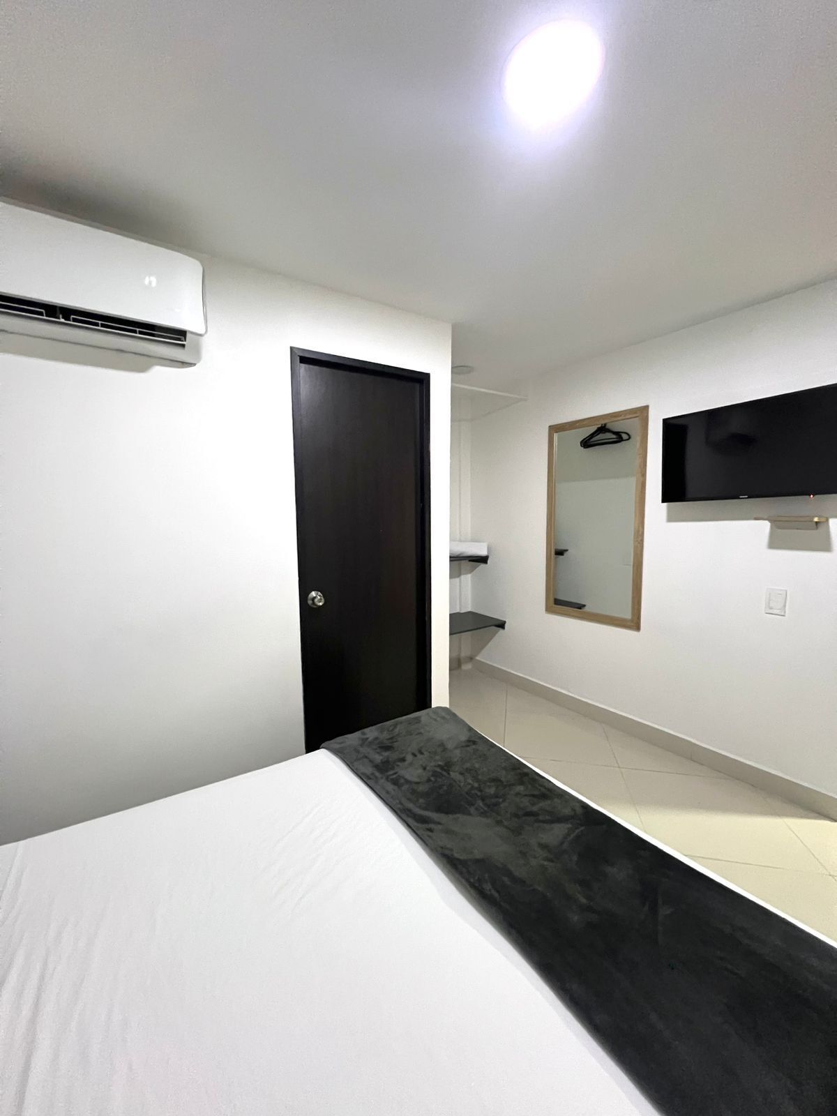 A bedroom with a bed, a dark door, a mounted TV, and a mirror on the wall.