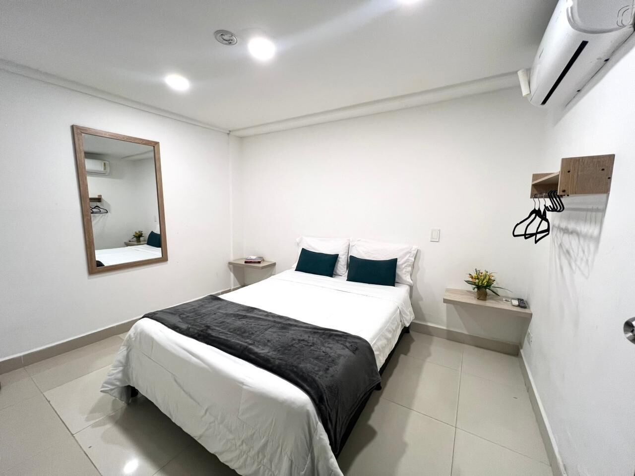 A neatly arranged bedroom with a bed, bedside table, and a mirror on the wall.