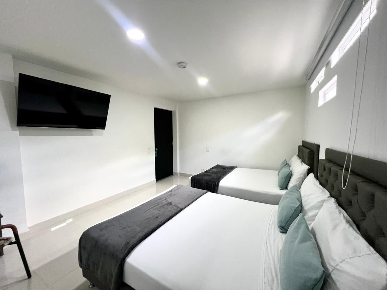 A modern hotel room with two beds, a flat-screen TV mounted on the wall, and a door leading to another room.