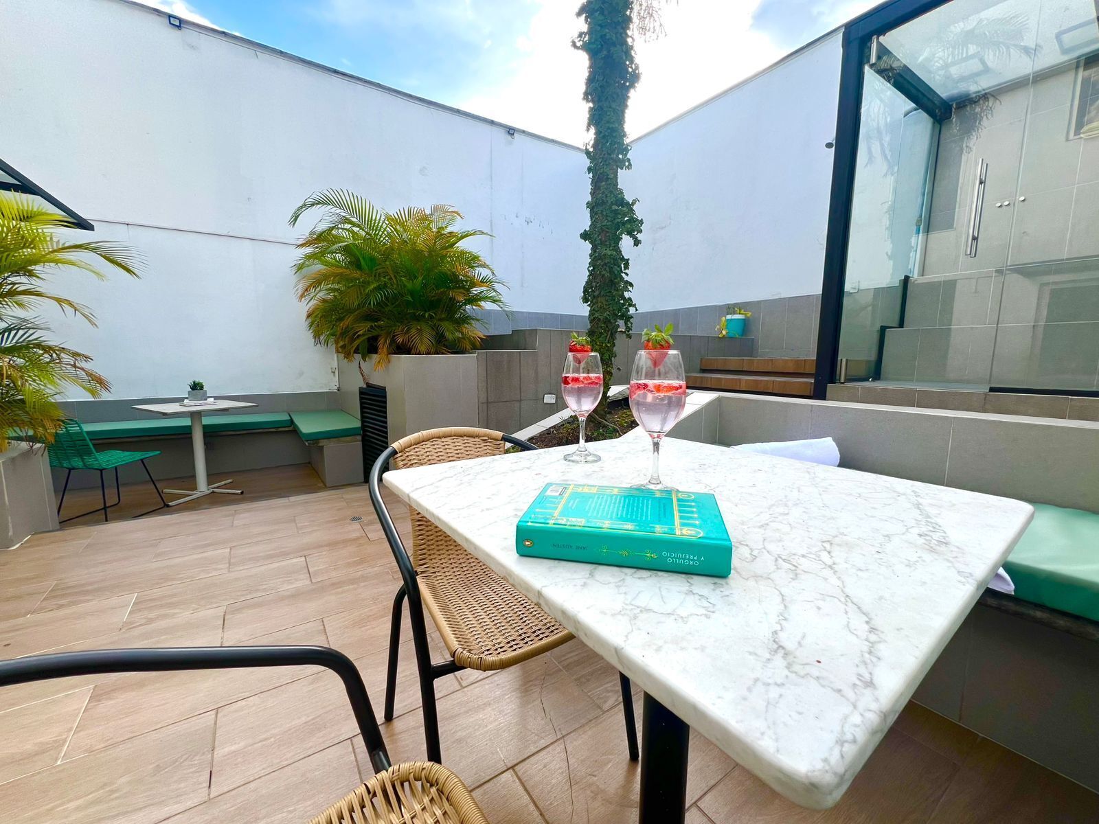 A patio with a marble table, wicker chairs, a green bench, and a potted plant.