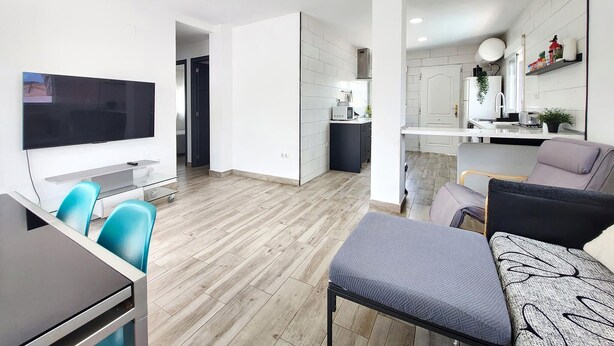 A modern living room with a flat-screen TV, a dining area with a table and chairs, and a kitchen with white cabinets and a microwave. - Stunning home in Turís (Turís)