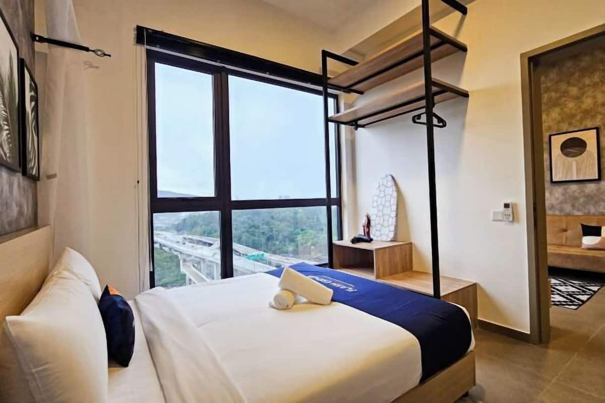A hotel room with a large window, a bed with a blue bedspread, a bedside table, and a hanging chair.