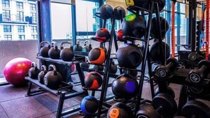 A gym with kettlebells and dumbbells on racks, a red exercise ball, and a window with a view of buildings. - Forte Seasons Mossaz Premium Suites Petaling Jaya by BYON (Petaling Jaya)