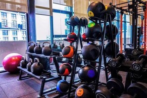Un gimnasio con pesas rusas y mancuernas en estantes, una pelota de ejercicios roja y una ventana con vista a edificios.
