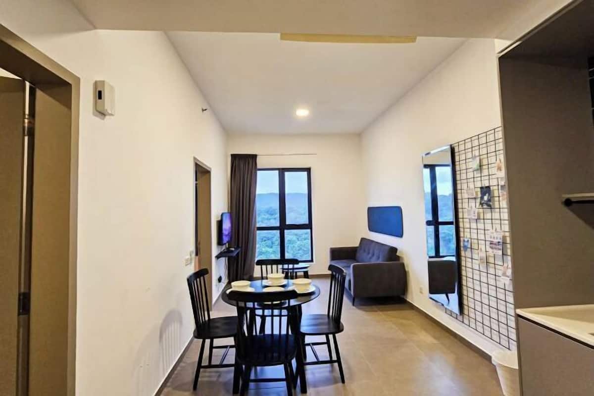 A modern hotel room with a dining area, a sofa, and a large window offering a view of the outdoors.
