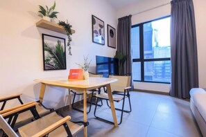 Una sala moderna con una mesa de comedor, sillas, un sofá, un televisor y un amplio ventanal con cortinas.