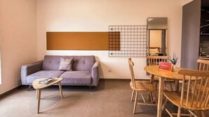 A living room with a sofa, coffee table, and dining area with chairs. - Forte Seasons Mossaz Premium Suites Petaling Jaya by BYON (Petaling Jaya)