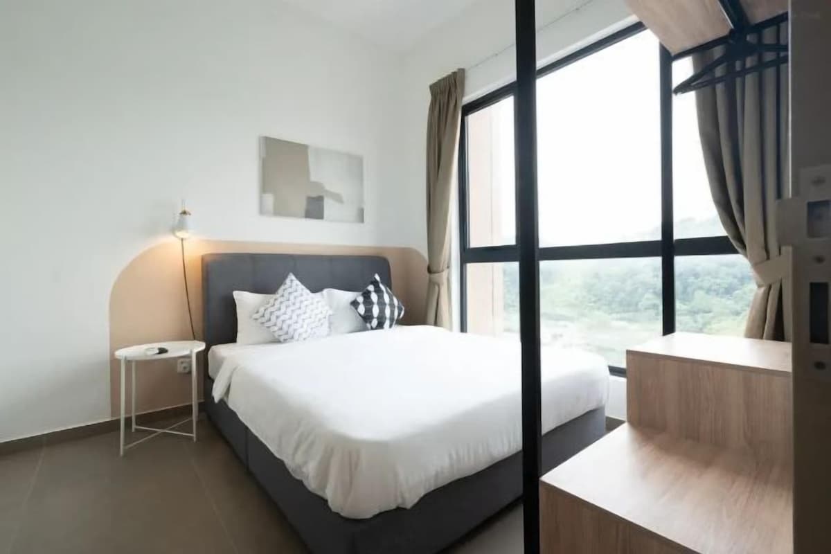 A modern hotel room with a large bed, a bedside table, a small side table, and a window with curtains.