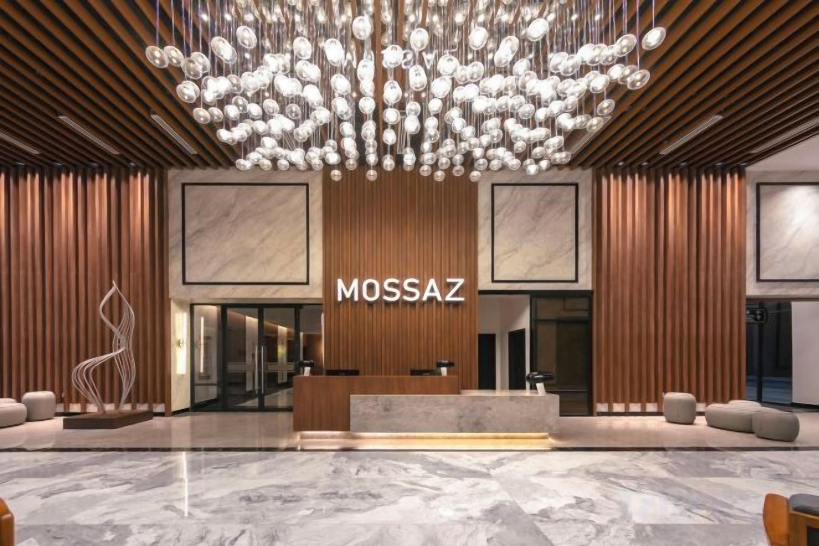 A reception area with a modern chandelier, a reception desk, and a sign that reads 'MOSSAZ'.