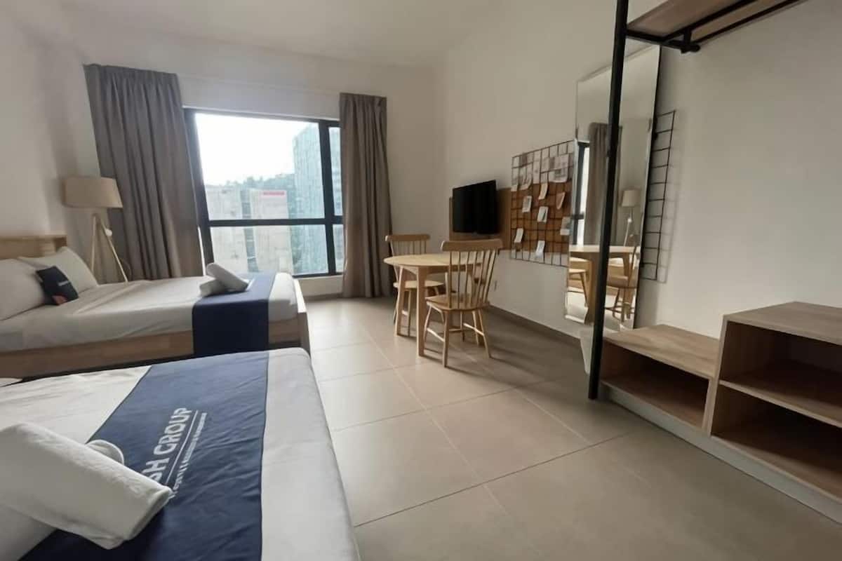A hotel room with two beds, a desk, a chair, a TV, and a large window.