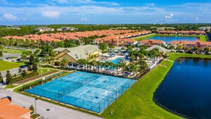 Un resort con varias edificaciones, una piscina grande, canchas de tenis y un lago.