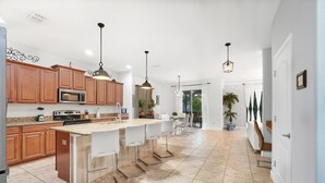 Una cocina moderna con armarios de madera, una isla central con taburetes de bar, electrodomésticos de acero inoxidable e iluminación colgante.