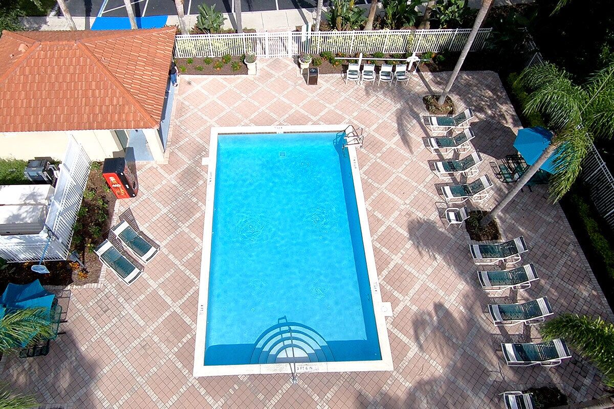 An aerial view of a swimming pool with lounge chairs and a fenced area.