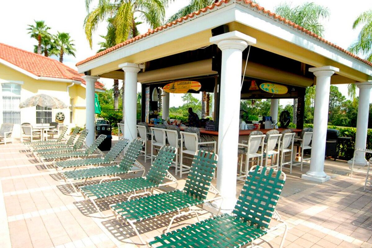 A covered outdoor seating area with green lounge chairs and a bar.