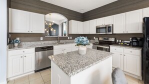 Una cocina moderna con armarios blancos, encimeras de granito y electrodomésticos de acero inoxidable, e una isla central.