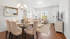 Un espace repas moderne avec une table en verre, des chaises de couleur beige et un lustre.